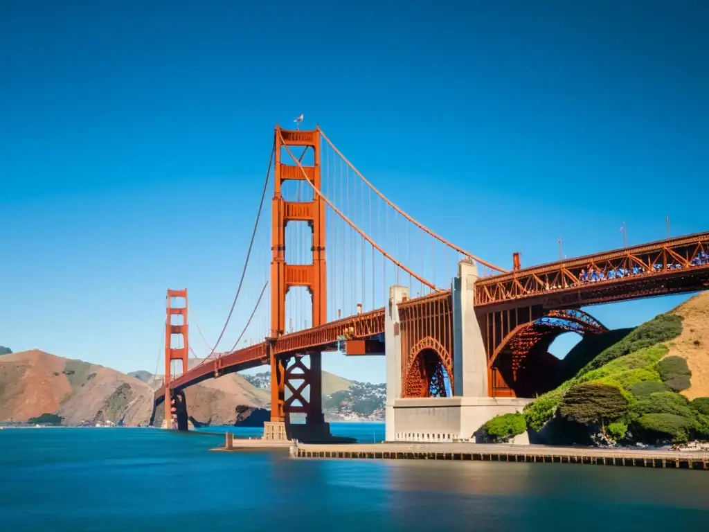 Imagen impactante del Puente Golden Gate en San Francisco, con sus torres rojo anaranjado sobresaliendo en el cielo azul y la estructura que atraviesa el agua, destacando su diseño arquitectónico y significado cultural en la sociedad contemporánea